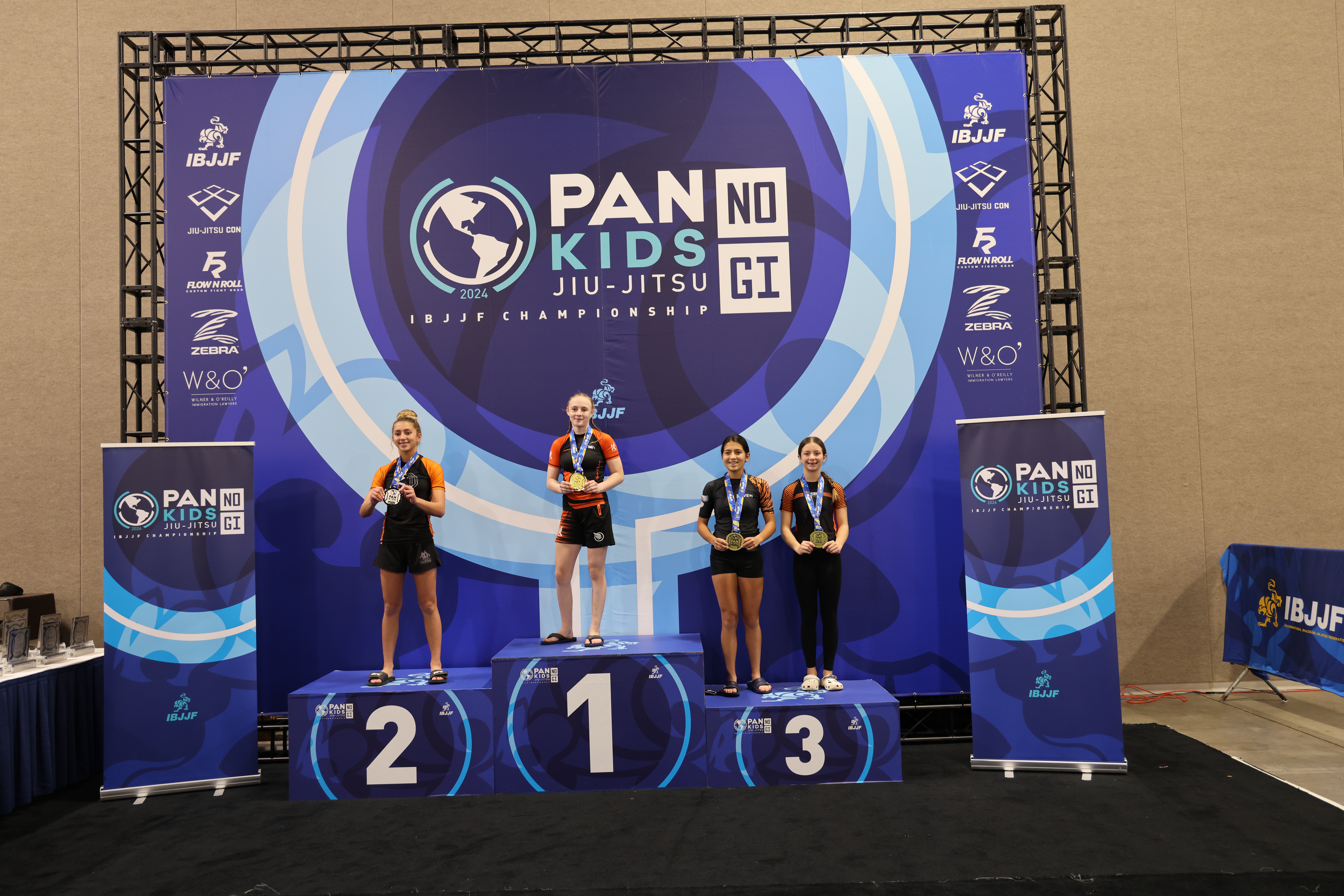 2024年 Pan Kids IBJJF No-Gi Championship の表彰台写真。表彰台の最上段には当該階級の優勝者が立っている。背景に大会ブランディングが見える: PAN KIDS NO-GI IBJJF CHAMPIONSHIP。