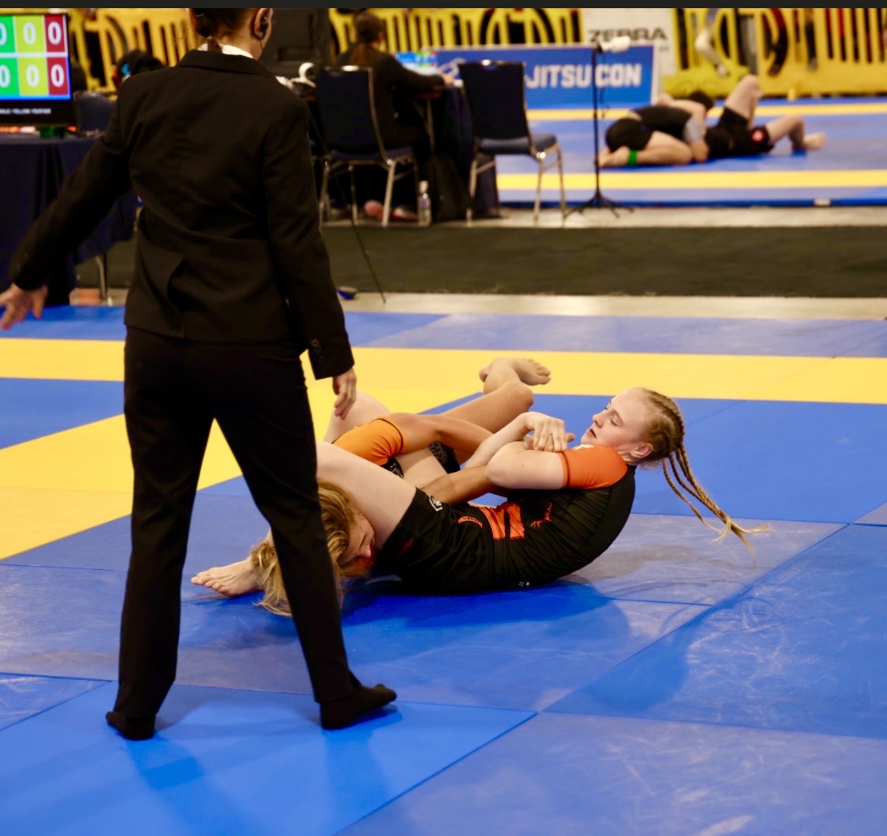 2024年 IBJJF Pan Kids No-Gi Championship のブラケットからの競技画像。被写体はトップコントロールのポジションにある。背景には採点テーブルと隣接するマットが見え、IBJJF 公認の競技環境であることがわかる。
